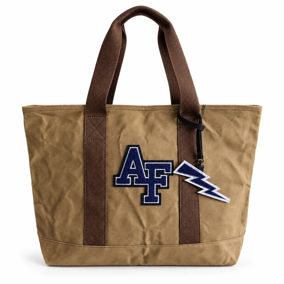 Tan Air Force Academy canvas boat tote with navy chenille AF patch, brown handles, and a navy lightning bolt bag charm attached to the handle.