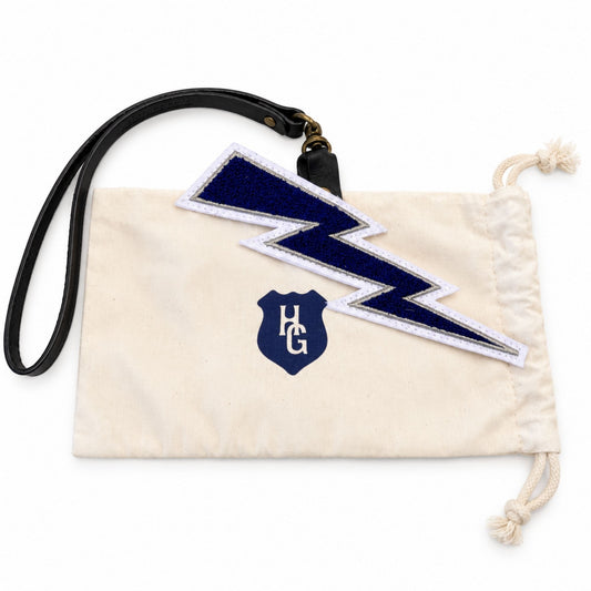 Navy blue Lightning Bolt Chenille Bag Charm with black leather strap displayed on a cream-colored Heritage Gear drawstring dust bag.