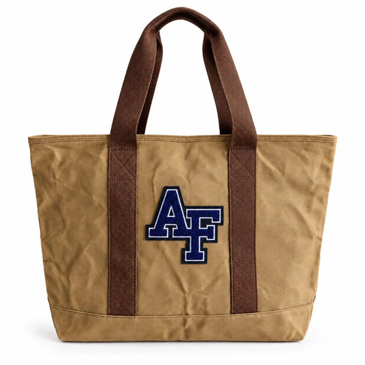Front view of the tan Air Force Academy canvas boat tote featuring a navy chenille AF patch, brown cotton handles, and structured canvas design.