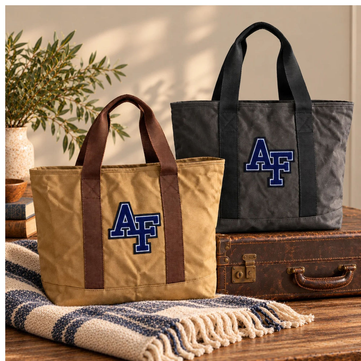 Tan and charcoal Air Force Academy canvas boat totes featuring chenille AF patches, styled with vintage luggage and a cozy blanket.
