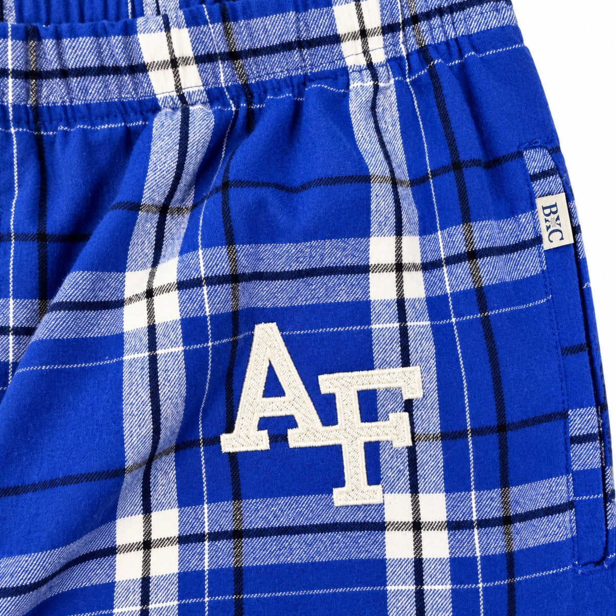 Close-up of white embroidered AF logo on royal blue plaid pajama pants, with waistband and side pocket detail.