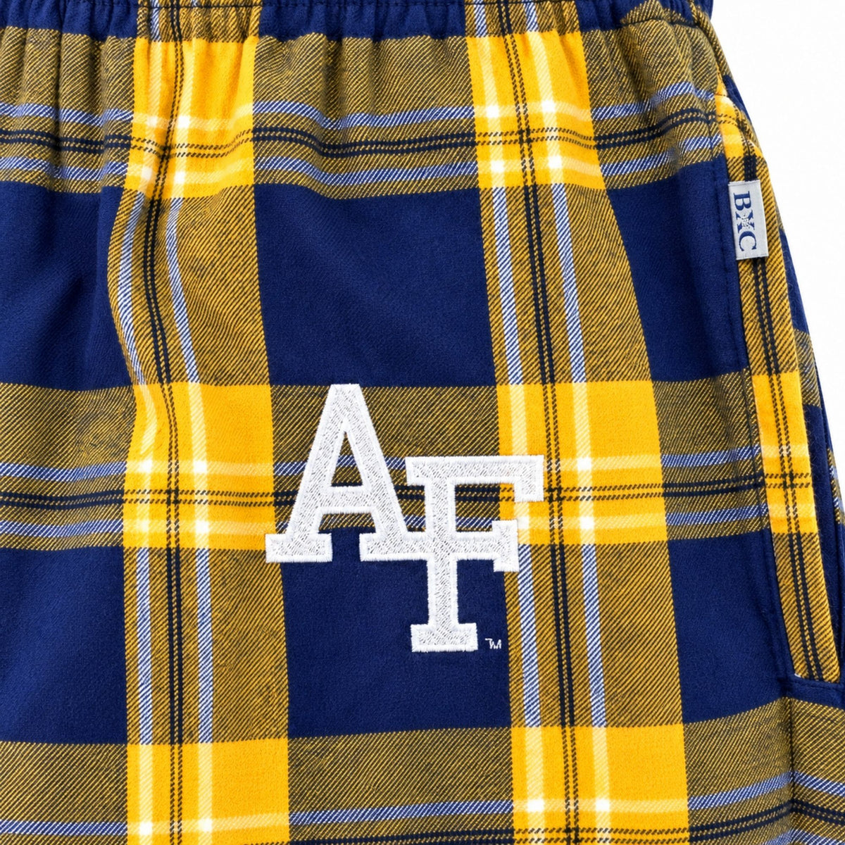 Close-up of white embroidered AF logo on gold and navy plaid pajama pants, with side pocket detail.