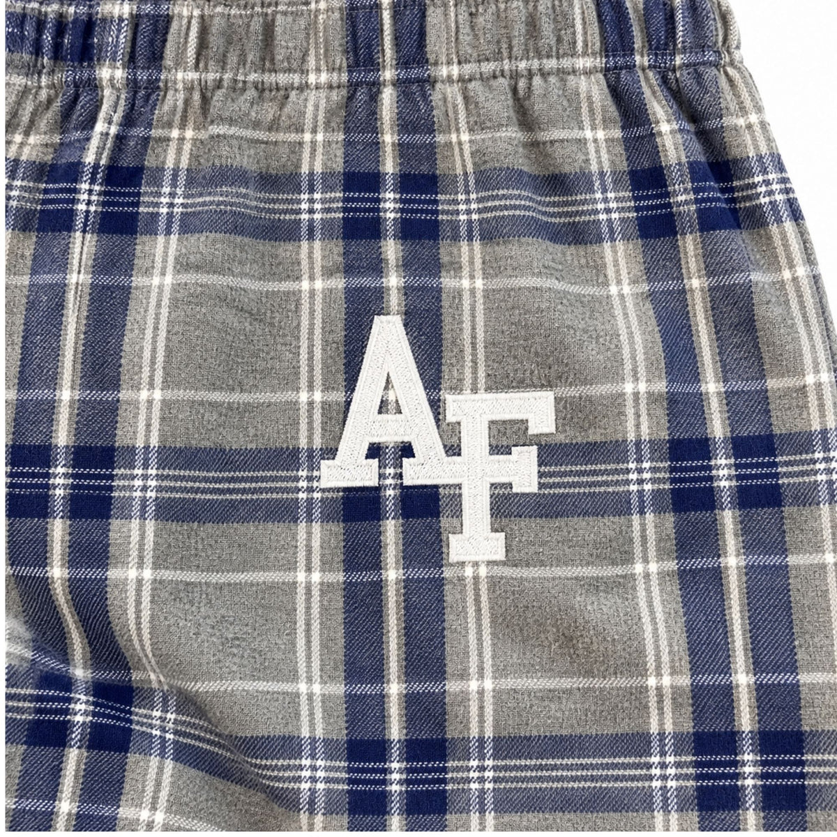Close-up of white embroidered AF logo on silver-gray pajama pants with navy and white plaid.